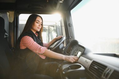 Büyük bir kamyonda oturan, kameraya bakıp gülümseyen güzel, genç kadın kamyon şoförünün portresi. Aracın içinde. İnsanlar ve ulaşım kavramı.