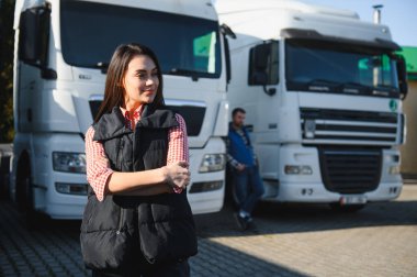 Kamyon şoförü mesleği. Kamyon araçlarının önünde günlük giysiler içinde duran kadın kamyon şoförünün portresi. Ulaştırma sektörü teması.