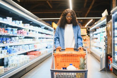 Afro-Amerikalı Kadın Müşteri Pozisyonu Dükkan Arabası ile Süpermarkette Gıda Ürünleri Alma, Kameraya Gülümseme. Siyahi Kadın Marketten Erzak Seçiyor