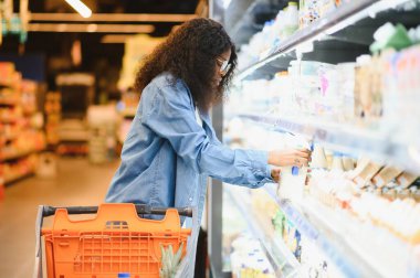 Afro-Amerikalı Kadın Müşteri Pozisyonu Dükkan Arabası ile Süpermarkette Gıda Ürünleri Alma, Kameraya Gülümseme. Siyahi Kadın Marketten Erzak Seçiyor