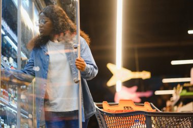 Afro-Amerikalı Kadın Müşteri Pozisyonu Dükkan Arabası ile Süpermarkette Gıda Ürünleri Alma, Kameraya Gülümseme. Siyahi Kadın Marketten Erzak Seçiyor