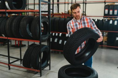 Otomobil satış departmanından yeni lastikler alırken marka ve ürün özelliklerini inceleyen genç adam portresi. Erkek müşteri araba aksesuarlarını seçiyor..