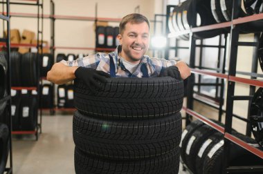 Neşeli ve komik lastik dükkânı çalışanı lastiklerin içinde oturup gülüyor..