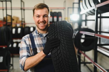 Gülümseyen depo çalışanının portresi yeni araba lastikleri yığınının yanında duruyor..