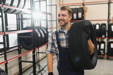 Araba lastiği servisi konsepti. Portre tamircisi arka planda yeni lastik tutuyor..