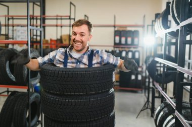 Neşeli ve komik lastik dükkânı çalışanı lastiklerin içinde oturup gülüyor..