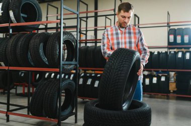 Otomobil satış departmanından yeni lastikler alırken marka ve ürün özelliklerini inceleyen genç adam portresi. Erkek müşteri araba aksesuarlarını seçiyor..