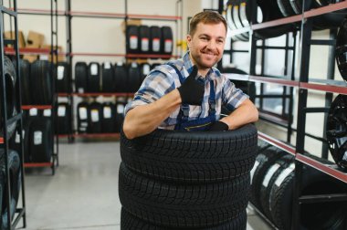 Neşeli ve komik lastik dükkânı çalışanı lastiklerin içinde oturup gülüyor..