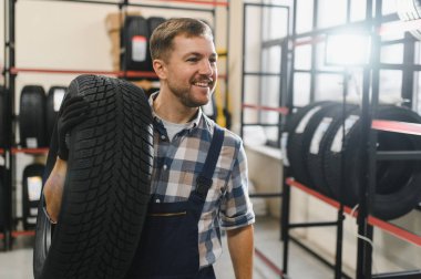 Gülümseyen depo çalışanının portresi yeni araba lastikleri yığınının yanında duruyor..
