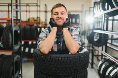 Neşeli ve komik lastik dükkânı çalışanı lastiklerin içinde oturup gülüyor..