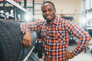 Afro-Amerikan adam araba tamirhanesinde kış lastiklerini seçiyor..