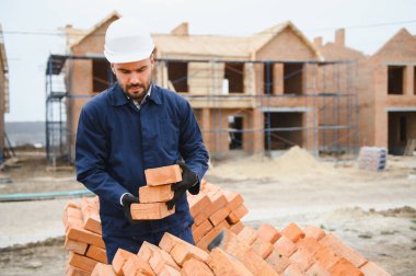 İnşaat alanındaki bir inşaatçının portresi. Tuğla evler inşa ediliyor.