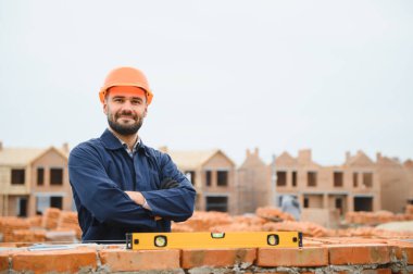 Tuğla duvar kuruluyor. Üniformalı inşaat işçisi ve güvenlik ekipmanı inşaatında çalışıyor.