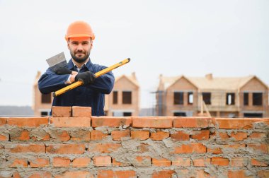 Tuğla duvar kuruluyor. Üniformalı inşaat işçisi ve güvenlik ekipmanı inşaatında çalışıyor.