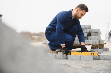 Eldivenlerin ustası katman katman taş döşüyordu. Profesyonel kaldırım işçisi tarafından kaldırım taşı döşenmiş. Kum temeli üzerine ev avlusunda gri beton döşeme döşeme döşeme döşeme.