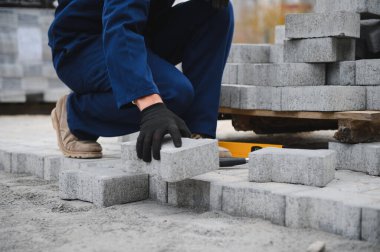 Eldivenlerin ustası katman katman taş döşüyordu. Profesyonel kaldırım işçisi tarafından kaldırım taşı döşenmiş. Kum temeli üzerine ev avlusunda gri beton döşeme döşeme döşeme döşeme.