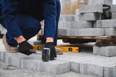 Eldivenlerin ustası katman katman taş döşüyordu. Profesyonel kaldırım işçisi tarafından kaldırım taşı döşenmiş. Kum temeli üzerine ev avlusunda gri beton döşeme döşeme döşeme döşeme.