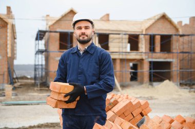 Tuğla duvar kuruluyor. Üniformalı inşaat işçisi ve güvenlik ekipmanı inşaatında çalışıyor.