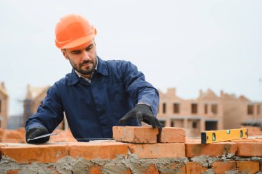 Tuğla duvar kuruluyor. Üniformalı inşaat işçisi ve güvenlik ekipmanı inşaatında çalışıyor.