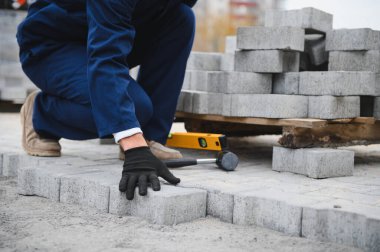 Eldivenlerin ustası katman katman taş döşüyordu. Profesyonel kaldırım işçisi tarafından kaldırım taşı döşenmiş. Kum temeli üzerine ev avlusunda gri beton döşeme döşeme döşeme döşeme.