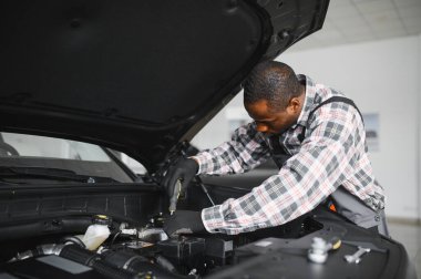 Afrikalı bir adam araba tamirhanesinde duruyor..