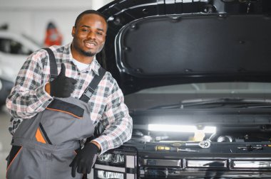 Afrikalı bir adam araba tamirhanesinde duruyor..
