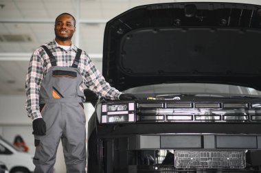 Afrikalı bir adam araba tamirhanesinde duruyor..