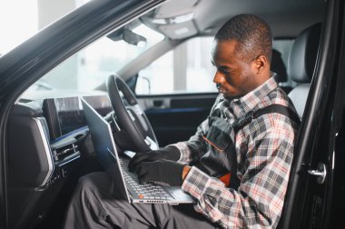 Black auto mechanic running diagnostic on laptop while analyzing engine problems in a workshop.