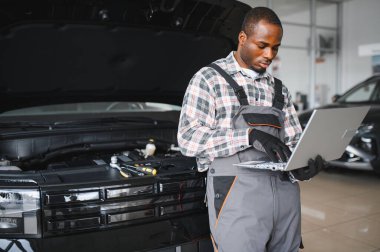 Araba servisindeki gülümseyen tamircinin portresi hasarlı araç için tablet kullanarak yeni parçalar sipariş ediyor. Bozuk arabalardaki eski parçaların yerine yenilerini arayan Afrikalı Amerikalı bir tamirci..