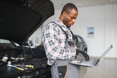 Araba servisindeki gülümseyen tamircinin portresi hasarlı araç için tablet kullanarak yeni parçalar sipariş ediyor. Bozuk arabalardaki eski parçaların yerine yenilerini arayan Afrikalı Amerikalı bir tamirci..