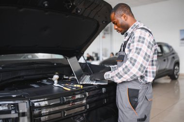 Araba servisindeki gülümseyen tamircinin portresi hasarlı araç için tablet kullanarak yeni parçalar sipariş ediyor. Bozuk arabalardaki eski parçaların yerine yenilerini arayan Afrikalı Amerikalı bir tamirci..