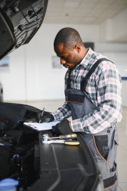 Araba servisi, onarım, bakım konsepti, atölyedeki panoya yazı yazan oto tamircisi, tamir makinesi için kontrol listesi hazırlayan teknisyen garajda bir araba, afiş..