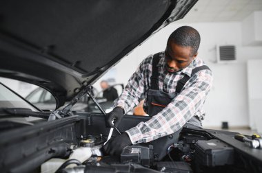 Afrikalı bir adam araba tamirhanesinde duruyor..