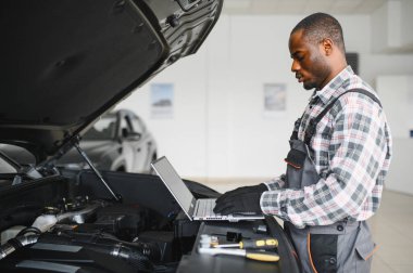 Afrikalı bir adam araba tamirhanesinde duruyor..