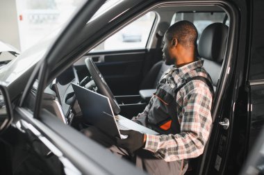 Black auto mechanic running diagnostic on laptop while analyzing engine problems in a workshop.