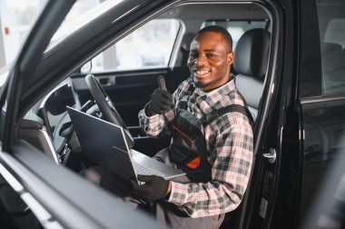 Araba servisindeki gülümseyen tamircinin portresi hasarlı araç için tablet kullanarak yeni parçalar sipariş ediyor. Bozuk arabalardaki eski parçaların yerine yenilerini arayan Afrikalı Amerikalı bir tamirci..