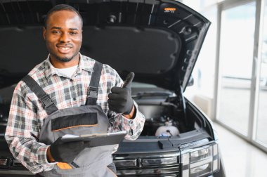 Engineer expertly examines car motor using advanced mechanical tools, ensuring optimal automotive performance and safety. African american garage employee conducts annual vehicle checkup. clipart