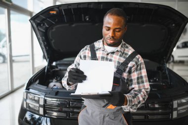 Afrikalı bir adam araba tamirhanesinde duruyor..