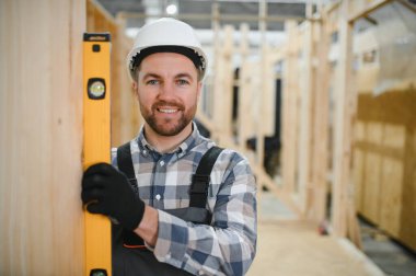 Kereste deposunda çapraz kollarla gülümseyen bir marangozun portresi, modüler yapı endüstrisinde uzmanlık gösteriyor..