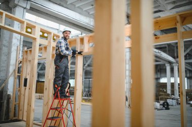 Kereste deposunda çapraz kollarla gülümseyen bir marangozun portresi, modüler yapı endüstrisinde uzmanlık gösteriyor..