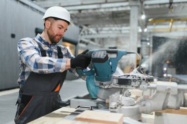 Bir marangoz modüler yapı fabrikasındaki kereste fabrikasında ahşap bir kereste keserek prefabrik bir yapı için hassas kesikler sağlar..