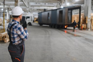 Foreman telsiz kullanarak prefabrik modüler bir evi kamyondan kamyona yüklüyor..