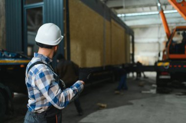 Bir işçi modüler evi kamyona yükleme işlemini kontrol eder. Ulaşım ve teslimat kavramı.