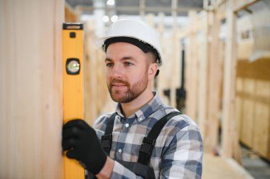 Üniformalı bir işçi ya da mühendis ahşap modüler evler için inşaat alanında çalışıyor..