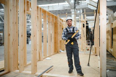 Modüler evlerin inşaat alanında miğfer takmış genç bir marangoz portresi..