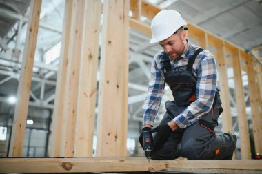 Kereste deposunda çapraz kollarla gülümseyen bir marangozun portresi, modüler yapı endüstrisinde uzmanlık gösteriyor..