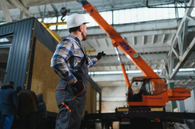 Foreman telsiz kullanarak prefabrik modüler bir evi kamyondan kamyona yüklüyor..