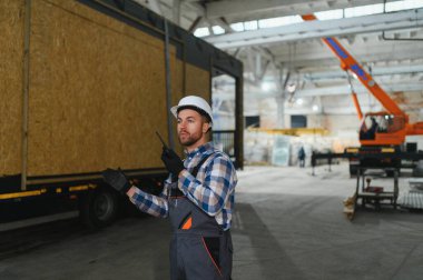 Foreman telsiz kullanarak prefabrik modüler bir evi kamyondan kamyona yüklüyor..