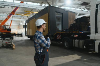 Foreman telsiz kullanarak prefabrik modüler bir evi kamyondan kamyona yüklüyor..