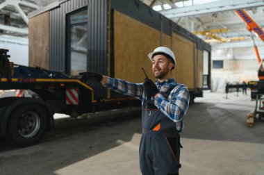 Foreman telsiz kullanarak prefabrik modüler bir evi kamyondan kamyona yüklüyor..